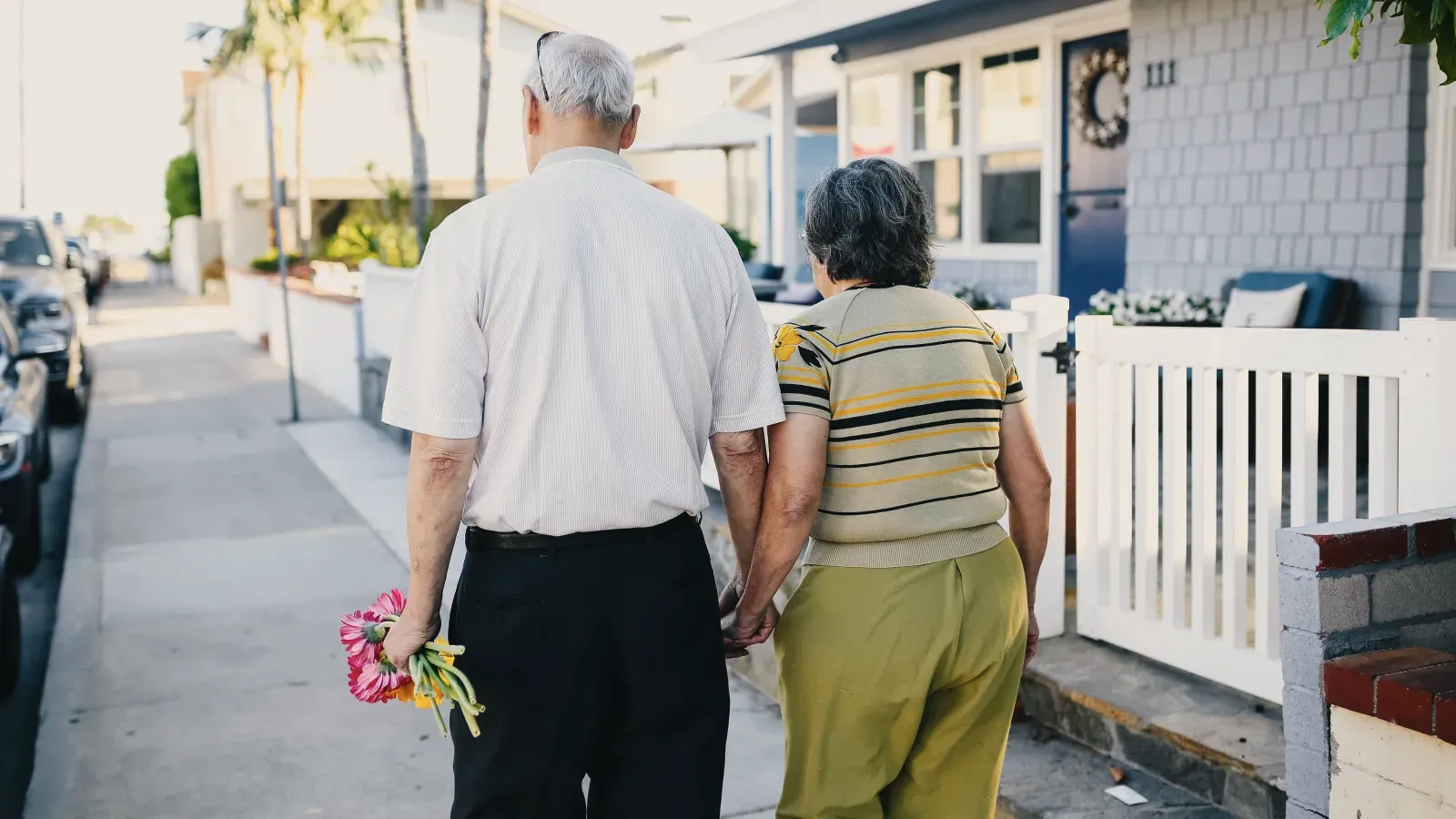 Two people walking hand in hand along a residential sidewalk, seen from behind.